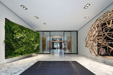 Das Zentrum des offenen, kreisförmigen Foyers bildet ein transparenter Windfang, der von feingerahmten automatischen Linearschiebetüren aus Wärmeisolierglas dominiert wird 
mit GEZE Slimdrive SL NT 